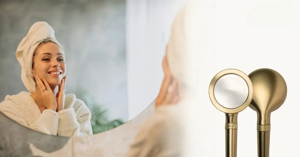 Woman with a towel wrapped on her head looking in the mirror, blu Ionic Shower Filter handheld alongside